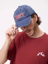 Gorro tipo dad hat de la marca Rusty, color azul con efecto gastado, visera curva y la palabra "RUSTY" bordada en relieve en el frente con letras rojas delineadas en blanco.