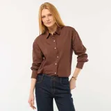Camisa de manga larga de popelina color marrón, con cuello camisero, cierre frontal de botones y puños anchos.