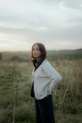 Saco tipo cardigan de punto color blanco con detalles de pespuntes decorativos en color negro a lo largo de los bordes y costuras. Presenta cuello en V, cierre frontal con botones y mangas largas.