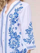 Blusa blanca con bordados florales en azul, de manga tres cuartos y cuello mao con escote en V.