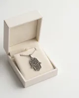 Dije de acero antialérgico con forma de mano de Hamsa, símbolo de protección y buena suerte, con detalles calados.