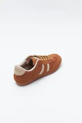Zapatilla urbana de perfil bajo con diseño retro, confeccionada en poliuretano con detalles en textura tipo gamuza. Presenta puntera redondeada, cordones clásicos y suela de goma color caramelo.