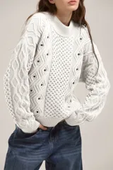 Sweater de punto color blanco con diseño de trenzas y rombos, cuello redondo y detalle de ojales metálicos distribuidos en el frente y las mangas.