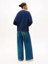 Buzo de felpa azul marino con cuello redondo, mangas largas y puños acanalados. Presenta un estampado frontal con el logo y letras de la marca Tommy Hilfiger en color blanco.