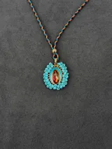 Collar con dije de la Virgen de Guadalupe rodeado de cuentas turquesas, con tira trenzada multicolor.