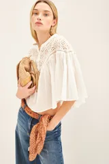 Camisa blanca de corte amplio y diseño cropped, confeccionada en algodón con detalles de encaje bordado en la parte superior y mangas acampanadas con textura rayada.
