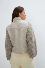 Campera de lana fina color crema, con cuerpo estructurado y mangas de tejido de punto acanalado. Presenta cuello alto, cierre frontal con botones y bolsillos laterales con doble abertura.
