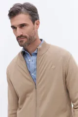 Campera de tejido de punto liviano color beige, con cierre frontal completo y cuello alto tipo bomber. Presenta un pequeño logo bordado en el pecho y puños acanalados.