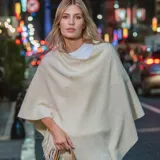 Poncho Fergie de tejido acrílico en color crudo, con diseño amplio y flecos en el borde inferior.