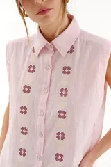 Chaleco camisero de algodón color rosado, sin mangas, con cuello camisero, cierre frontal de botones y detalles de bordado en punto cruz a lo largo del frente.