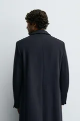 Abrigo de corte regular fit confeccionado en tejido de mezcla de lana de origen italiano. Presenta cuello con solapas de pico, cierre frontal de botonadura cruzada, mangas largas con puños abotonados y bolsillos con solapa en la cadera. Incluye detalle de bolsillo interior y abertura central en la espalda.