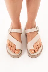 Sandalias de cuero color arena, con diseño de tiras cruzadas, sujetador para el dedo y hebilla metálica lateral. Cuenta con suela acolchada y plataforma plana forrada.