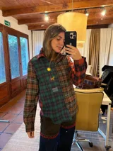 Camisa de corte amplio confeccionada en tela suave con diseño de paneles en diferentes estampados de cuadros escoceses en tonos verde, rojo y marrón. Presenta detalles bordados en el frente que incluyen un sol, un caballo y una bandera. Cuenta con cuello clásico y cierre frontal con botones.