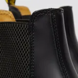 Bota Chelsea Dr. Martens modelo 2976, confeccionada en cuero liso negro con inserciones elásticas laterales, tirador en el talón y suela con cámara de aire reforzada con pespunte amarillo característico.