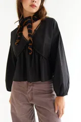 Blusa blanca de algodón con diseño de escote en V, mangas largas abullonadas y detalle de frunces en el frente y la espalda.