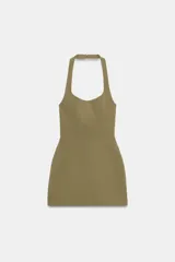 Vestido corto de color verde militar, con cuello halter, hombros descubiertos y costuras marcadas que aportan estructura. Cierre posterior con cremallera.