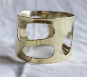 Brazalete rígido de bronce color dorado con diseño calado irregular.