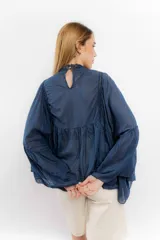 Camisa de algodón con diseño romántico, mangas amplias y detalles de puntillas verticales en el frente. Presenta un corte holgado y fluido.