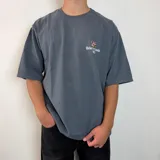 Remera negra de corte oversize con estampa gráfica en la espalda que presenta un oso con anteojos y bandana, acompañada de la frase 'Richer, Louder & Unbothered Than Ever'.