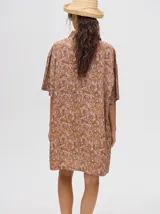 Camisa tipo vestido de corte oversize, confeccionada en viscosa. Presenta un diseño estampado con trazos abstractos en tonos verdes sobre una base naranja, cuello clásico, cierre frontal con botones y mangas cortas.