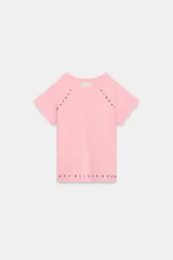Camiseta de algodón en color rosado con cuello redondo y manga corta. Presenta un diseño decorativo con tachas metálicas en forma de estrellas y puntos distribuidas en las costuras de los hombros y en el ruedo inferior.
