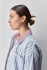 Camisa de calce relajado con diseño a rayas verticales en tonos azul y blanco, cuello clásico, mangas largas con puños abotonados y cierre frontal con botones. Presenta bolsillos aplicados en el delantero y una silueta versátil.
