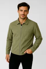 Campera de algodón color verde oliva, con cierre frontal completo, cuello clásico y dos bolsillos frontales tipo parche en el pecho. Presenta un diseño de corte recto y mangas largas con puños abotonados.