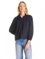Blusa de gasa con plisado soleil, cuello a la base fruncido con escote en V regulable mediante lazos, y mangas largas abullonadas con puños sastreros.
