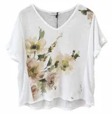 Blusa blanca de lino con escote en V, mangas cortas con vuelta y diseño asimétrico más largo en la parte trasera. Cuenta con un delicado estampado floral en tonos verdes y nude en el frente y en el hombro.