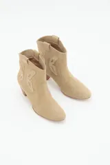 Bota corta estilo texano con taco medio de 6 cm. Confeccionada en cuero gamuzado, presenta recortes laterales que emulan la forma de una mariposa. Diseño de punta fina y caña media.