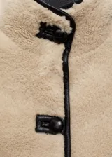Chaqueta de efecto pelo en color beige, con diseño oversize y corte recto. Presenta cuello alto, cierre frontal con botones y detalles de ribetes en cuero sintético negro.
