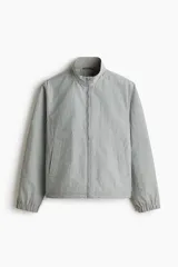 Campera rompevientos de nylon color gris, repelente al agua, con cuello elevado, cierre frontal y bolsillos laterales con botón a presión oculto.