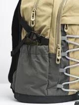 Mochila color arena con detalles en gris y negro. Cuenta con un compartimento principal con cierre, un bolsillo frontal con cordón elástico y bolsillos laterales de malla.