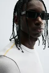 Camiseta de corte relajado, color gris claro, confeccionada en tejido con estructura waffle. Presenta cuello redondo y manga corta, con costuras decorativas en contraste color dorado que recorren los laterales y los hombros.