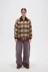 Campera de estilo bomber con cierre frontal, confeccionada en tejido a cuadros en tonos marrones y beige. Presenta cuello camisero en pana marrón, puños y ruedo elásticos acanalados, y bolsillos laterales.