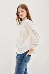 Camisa negra de algodón con cuello alto, cierre frontal de botones y detalles de encaje vertical y en los puños.