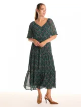 Vestido midi de gasa estampada en tonos verdes y marrones, con escote en V cruzado en la parte delantera y escote redondo elastizado en la espalda. Presenta cintura elastizada con lazo fino para anudar, mangas cortas evasé con volumen y falda con volados escalonados. Incluye forro interno a tono.