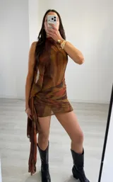 Vestido corto sin mangas en tonos marrón, naranja y tostado, con diseño estampado efecto degradado, cuello halter y detalle drapeado en la cintura con una tela lateral caída.