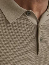Polo de punto estructurado color greige, con cuello clásico, cierre frontal de dos botones y mangas cortas con terminación acanalada.