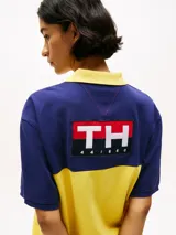 Chomba Tommy Hilfiger de corte amplio, con diseño color block en azul y amarillo, cuello clásico, cartera de tres botones, logo bordado en el pecho y logo oversize en la espalda.