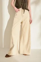 Jeans de corte wide leg, tiro alto y color beige, con detalles de costuras desflecadas a lo largo de las piernas.