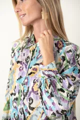Camisa de satén estampada con motivos geométricos en tonos lila, celeste, verde y amarillo. Tiene cuello clásico, mangas largas con puños abotonados y cierre frontal con botones.
