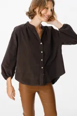 Camisa de pana color verde oliva, con cuello mao, cierre frontal de botones y mangas largas abullonadas con puños elásticos.