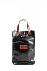 Bolso matero negro de cuero charolado con manijas cortas marrones y bolsillo frontal con cierre de gancho.