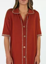 Vestido midi de punto color beige, con cuello solapa, mangas cortas y cierre frontal con botones. Presenta detalles de costuras y terminaciones en color mostaza, además de un diseño calado en el sector inferior de la falda.