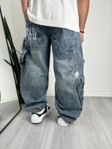 Pantalón de jean estilo baggy con lavado ácido, corte holgado y diseño bordado con temática de telarañas y arañas en los bolsillos traseros.