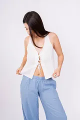 Chaleco corto sin mangas color verde salvia, confeccionado en tela perforada (broderie o calado). Presenta escote en V con lazos ajustables en el centro frontal.