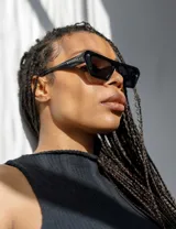 Lentes de sol negros con marco rectangular grueso y patillas anchas.