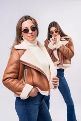 Campera tipo gamulán de cuerina color camel, con interior y detalles en corderito sintético color crema. Presenta diseño biker con cierre diagonal, cuello amplio con solapas y puños con forro de corderito.