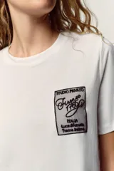Camiseta blanca de manga corta y cuello redondo, con aplicación de organza y texto negro a contraste en el pecho.